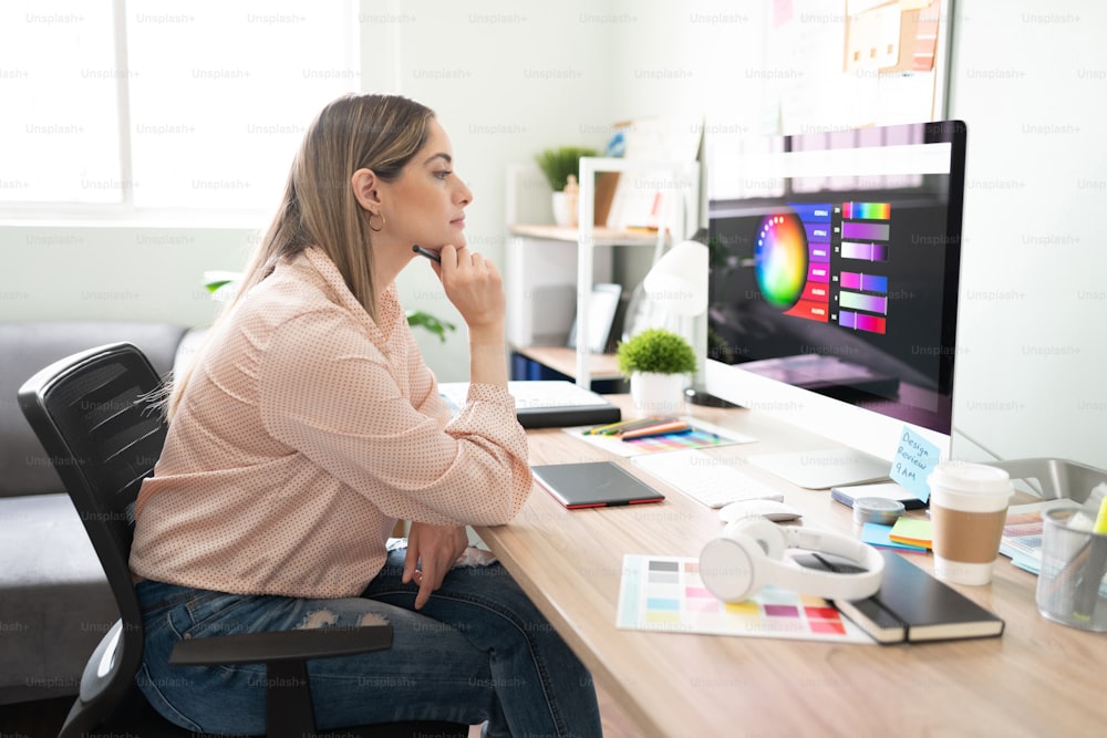 Pretty Caucasian woman and freelance graphic designer feeling thoughtful and looking at her computer screen
