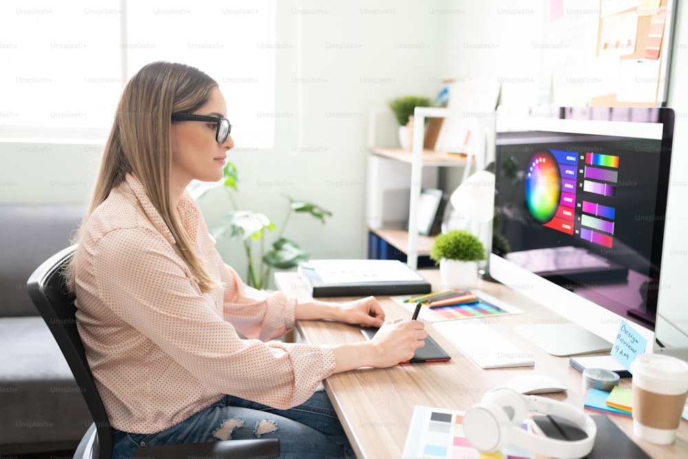 Profile view of a female illustrator wearing glasses and working on a drawing using a graphic tablet