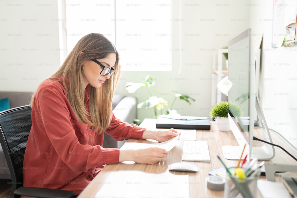 Busy female translator reading and reviewing a couple of documents in her office