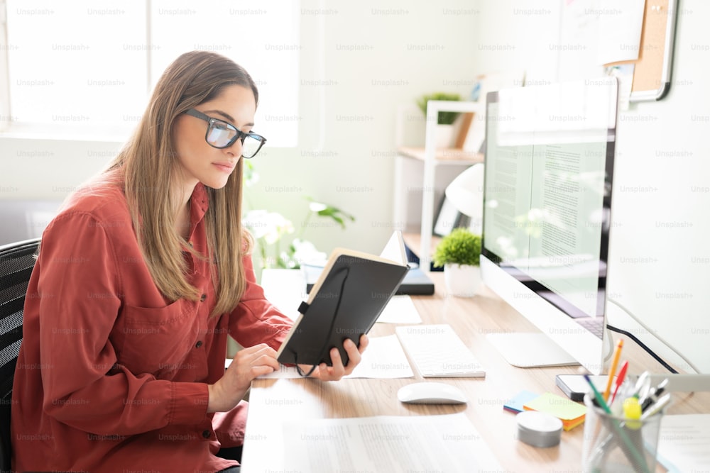 Serious and confident freelance writer checking her notes on a notepad and looking very busy and focused in an office