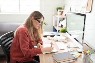 Beautiful woman and writer taking some notes in a notepad and filling the desk with crumpled paged due to her lack of inspiration