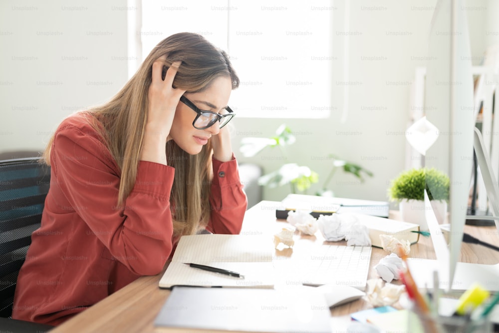 L’écrivaine stressée se sent coincée en essayant de trouver de nouvelles idées pour son livre à son bureau avec de nombreux papiers froissés