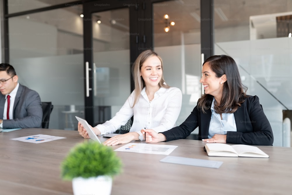 Businesswomen smiling while discussing work together in office boardroom