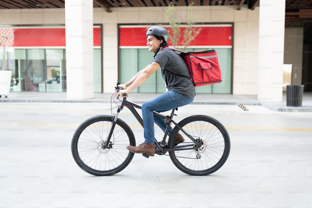Giovane ispanico sorridente fuori per la consegna in bicicletta in città
