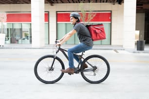 Joven hispano sonriente sale a entregar en bicicleta en la ciudad