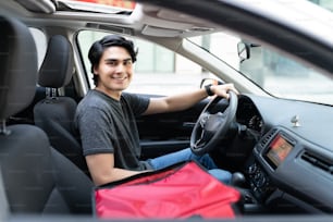 Sonriente joven repartidor guapo conduciendo coche