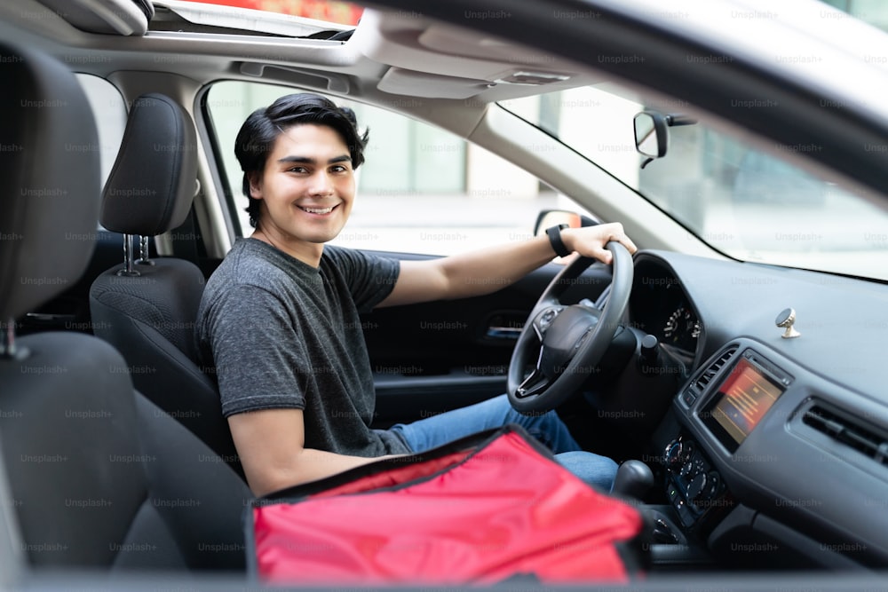 Smiling good looking young delivery man driving car