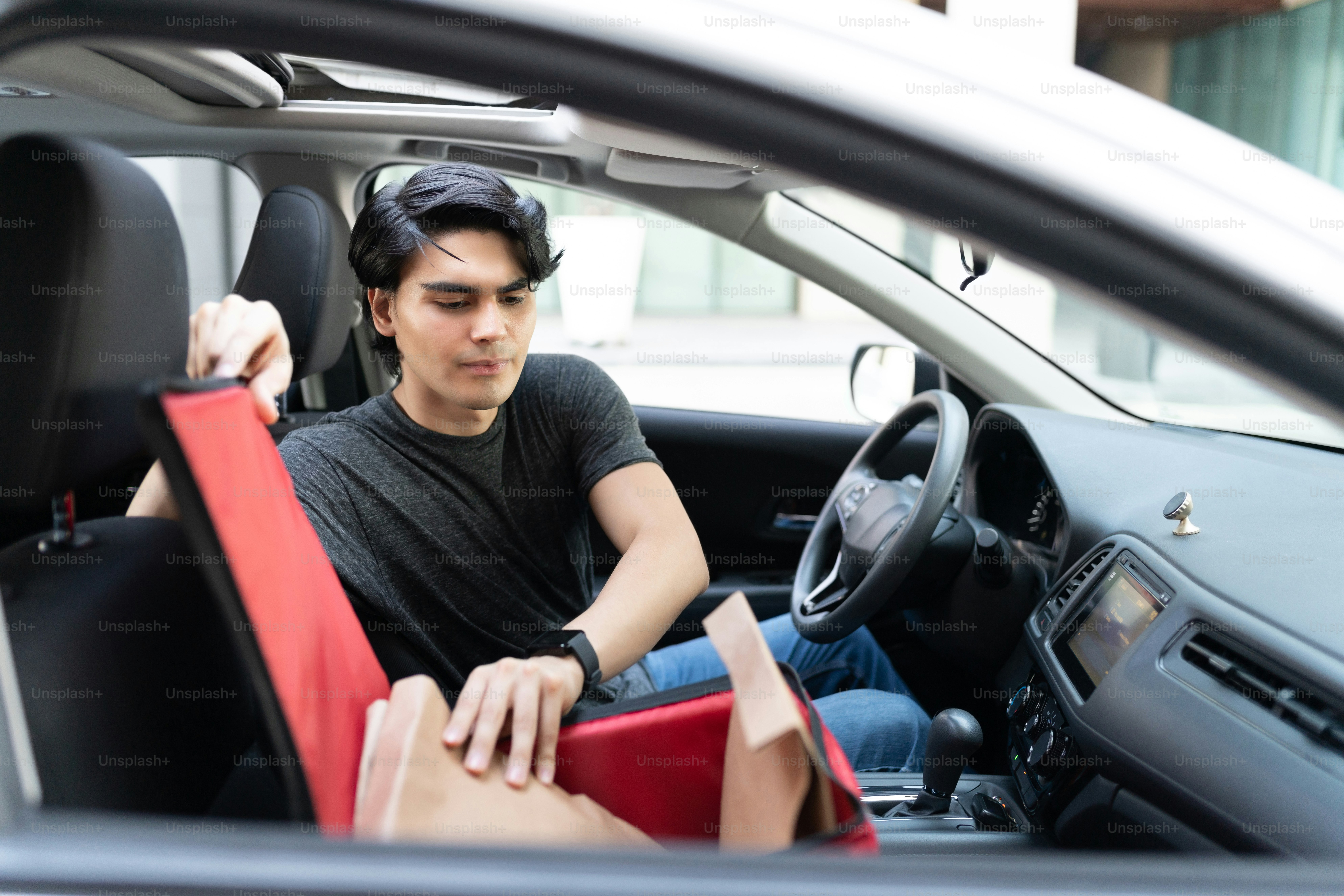 Joven repartidor hispano retirando paquete de mochila en auto