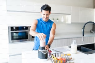 Hombre activo guapo preparando batido de fresa en la cocina antes de hacer ejercicio