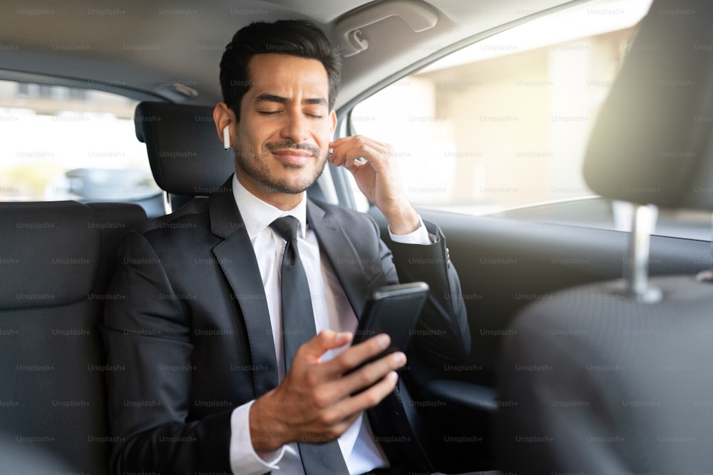 Giovane uomo d'affari ispanico che ascolta la musica attraverso gli auricolari wireless mentre viaggia in auto