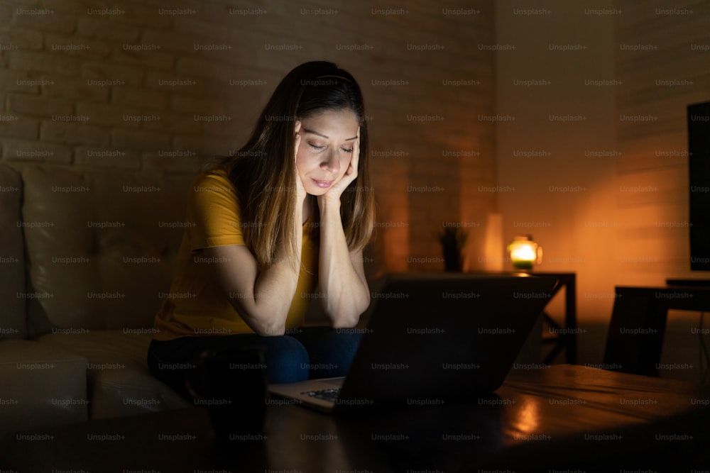 Donna bruna che si sente sopraffatta dal lavoro e dallo stress di notte mentre lavora da casa su un computer portatile