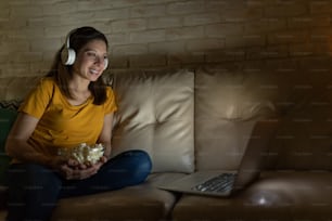 Ritratto di una bella donna che si gode la serata al cinema a casa usando cuffie e un computer portatile e sorridente