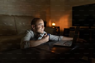 Retrato de un hombre guapo relajándose y viendo un programa de televisión o una película en una computadora portátil por la noche