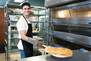 オーブンから一斤のパンを取り出し、微笑むハンサムな男性のパン屋のポートレート
