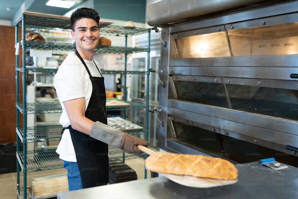 Retrato de un apuesto panadero sacando una hogaza de pan del horno y sonriendo