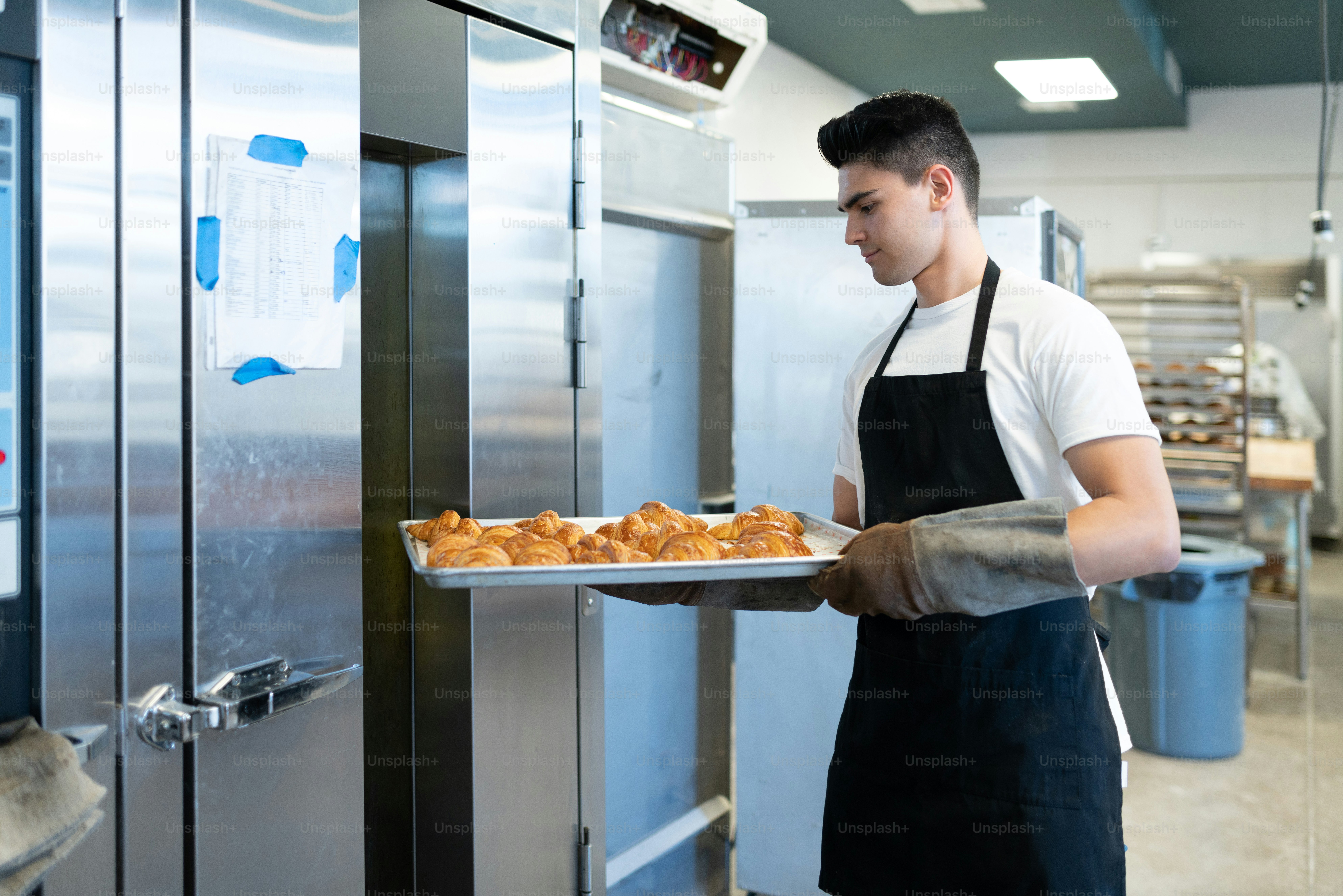 Good looking male baker holding a tray of freshly baked bread after taking it out of the oven