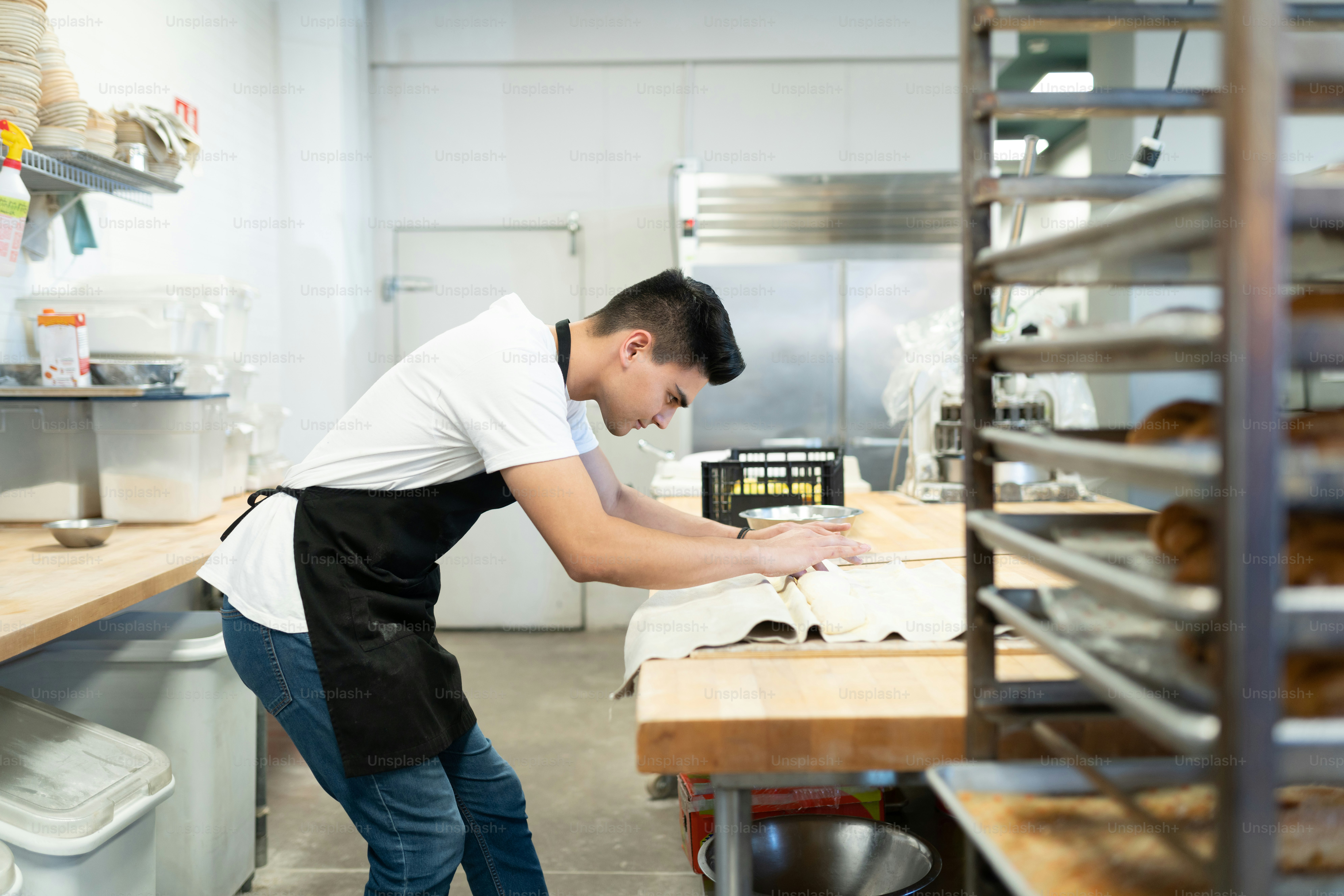 Profile view of a focused baker preparing some dough in the kitchen and enjoying his work