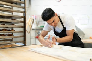 Focused male baker working with dough and making a few loaves of bread in a bakery
