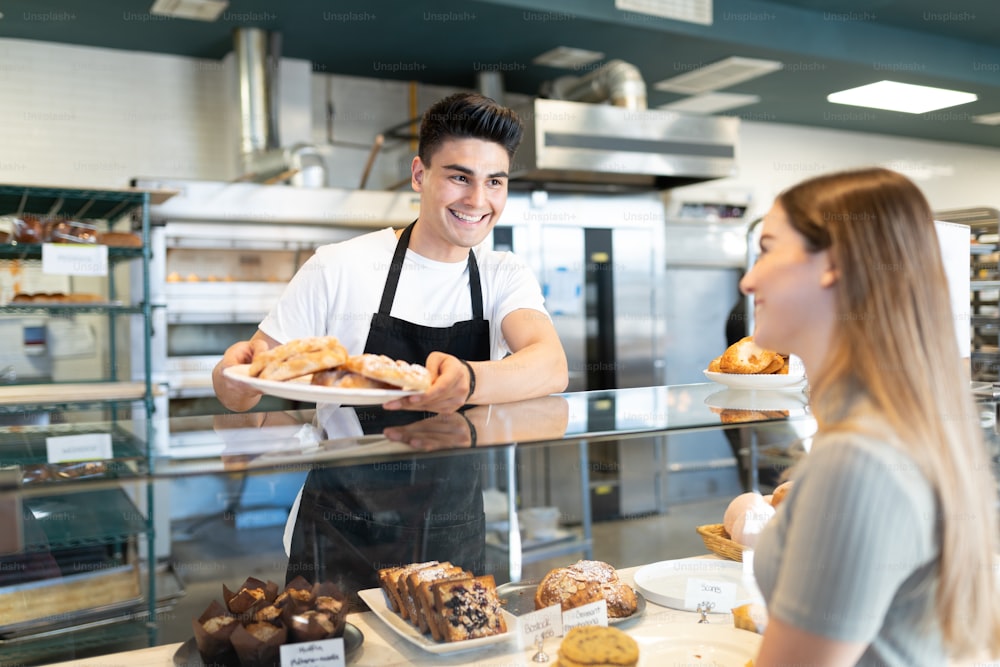 Attractive male baker showing a plate of pastries to a customer and giving her some options