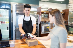 Young Caucasian woman paying at a bakery shop with her smartphone at the checkout counter