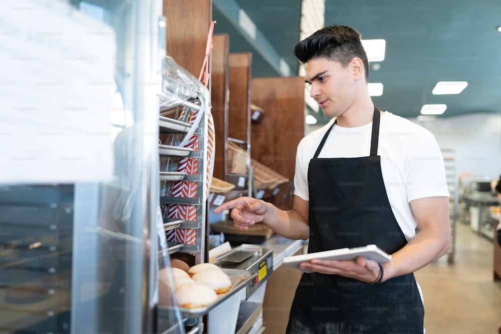 Good looking male worker using a tablet computer to do inventory in a bakery shop