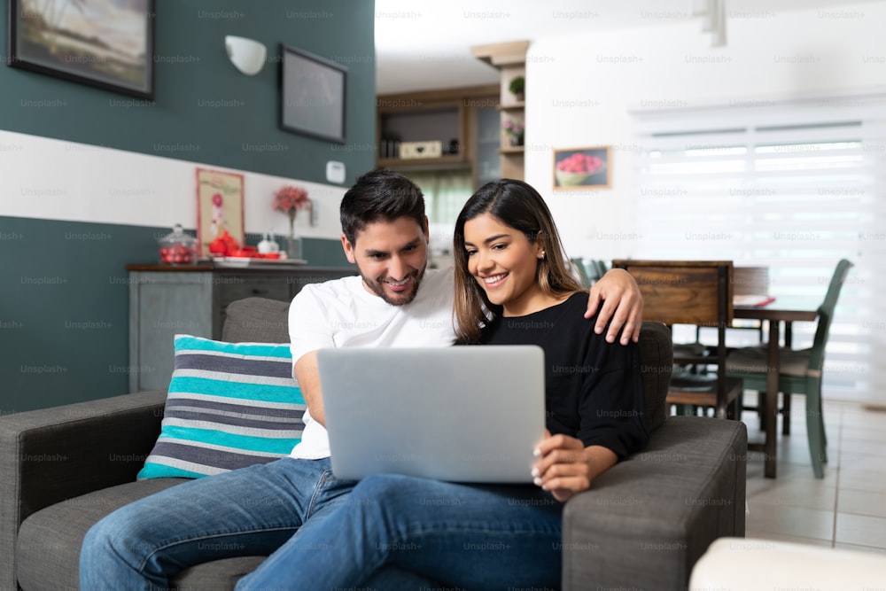 Happy Hispanic couple using laptop while sitting on couch in living room at home