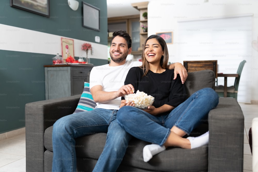 Hispanic couple eating popcorn while watching movie in living room at home