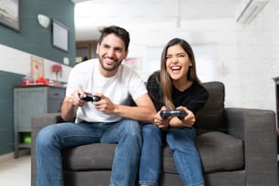 Uomo e donna latini felici che giocano al videogioco mentre sono seduti sul divano a casa