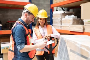 Confident supervisor examining list while standing by coworker at factory