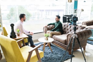 Male reporter sitting with young professional while recording interview in office