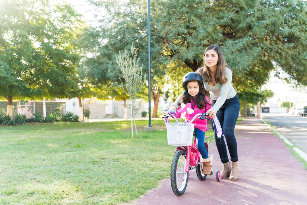 Madre ayudando a su hija a andar en bicicleta en la acera del parque