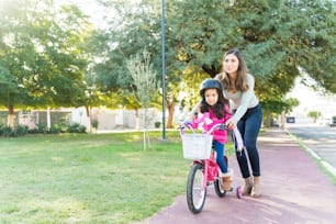 Une mère aide sa fille à faire du vélo sur le trottoir du parc
