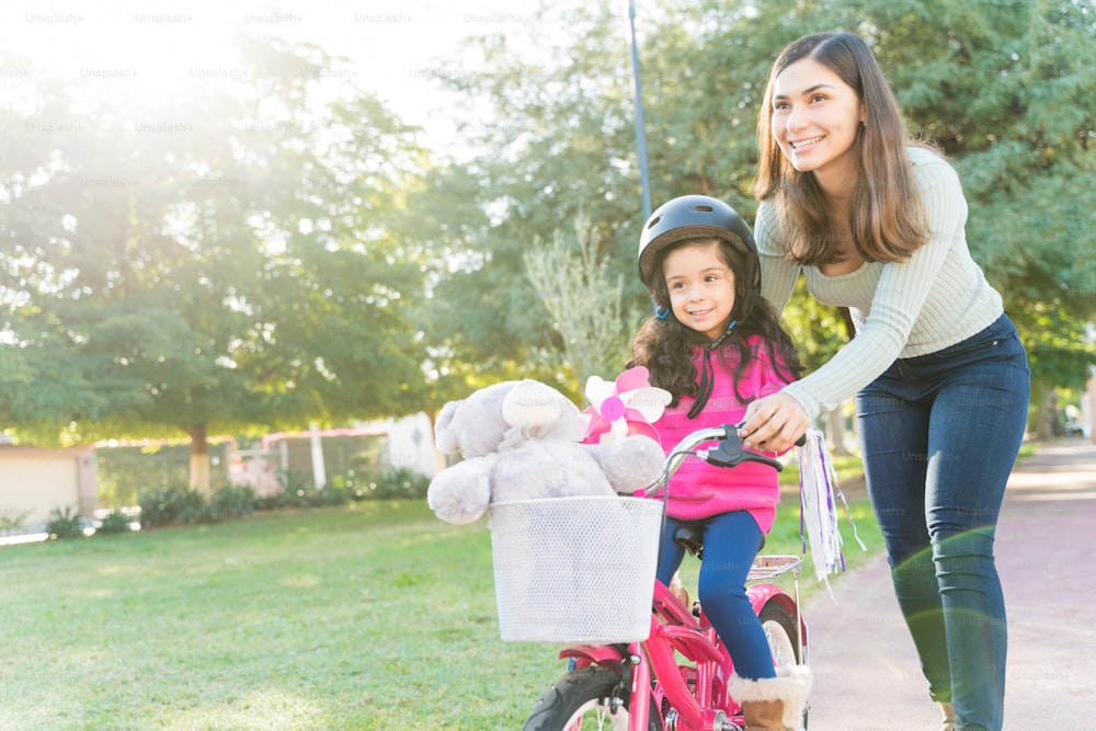 Madre hispana sonriente enseña a su hija a andar en bicicleta en el parque durante el fin de semana