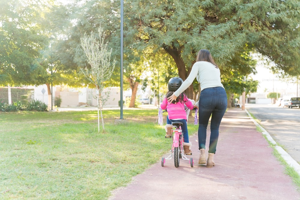 公園の歩道�で自転車に乗る娘を導く母親の背面図