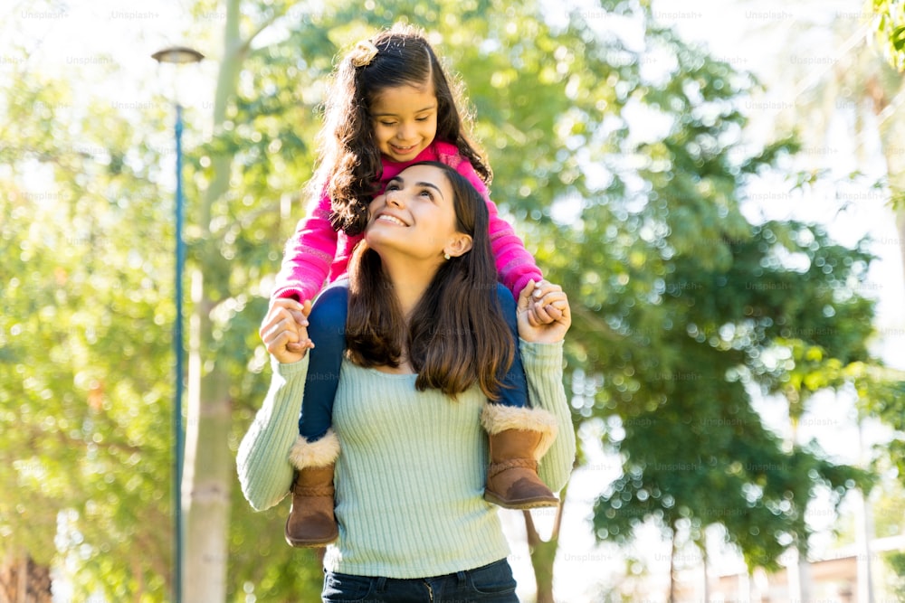 Gorgeous Latin Mother Looking At Daughter While Carrying Her On Shoulders During Weekend