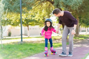 Cuerpo entero de hombre sosteniendo la mano de su hija mientras ayuda a patinar en la acera en el parque