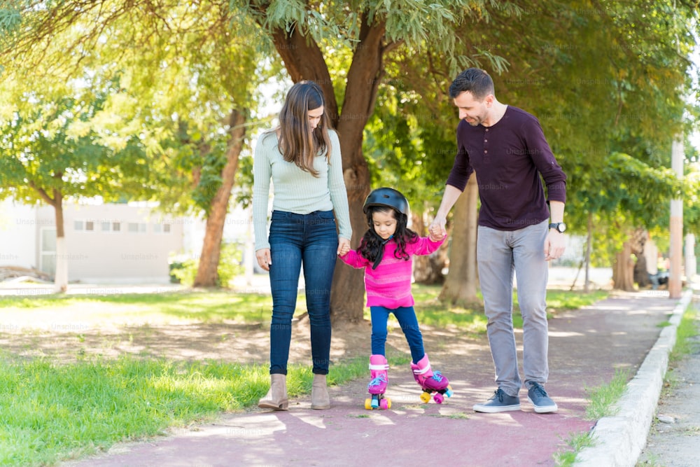 Hispanic Father And Mother Holding Daughter'S Hand While Guiding To Skate On Sidewalk