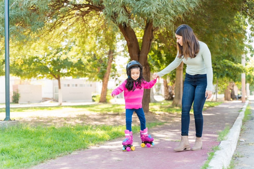 Une mère guide sa fille en patinant sur le trottoir du parc