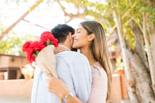 Happy attractive Latin woman holding flowers while embracing boyfriend