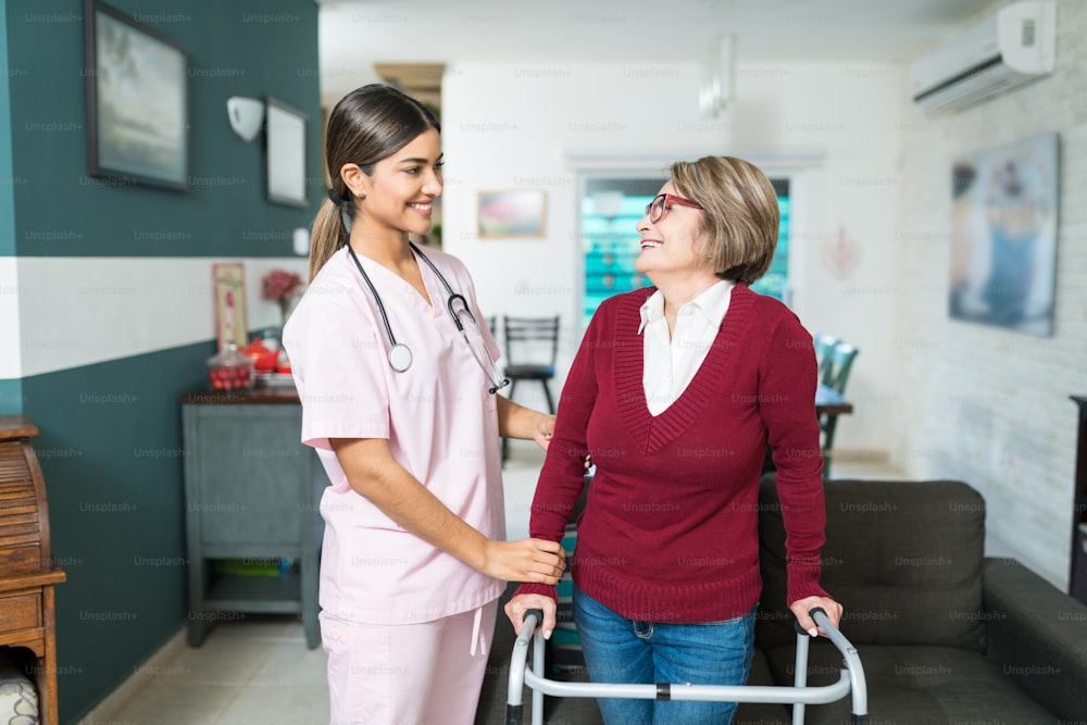 Smiling female nurse helping senior woman to walk with mobility walker at home