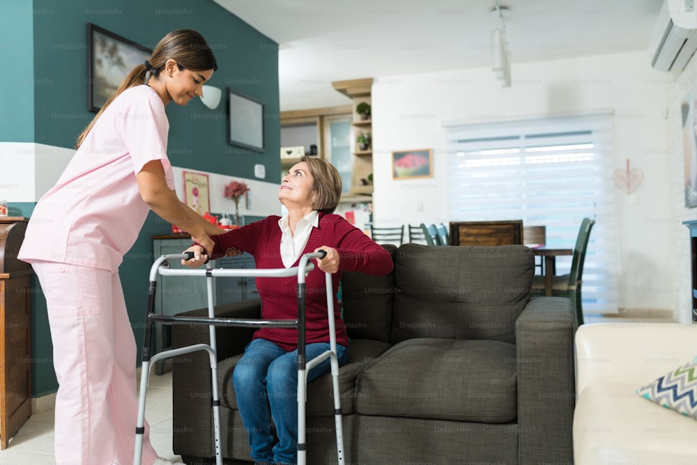 Enfermeira confiante que ajuda a mulher com deficiência sênior a andar com andador de mobilidade em casa