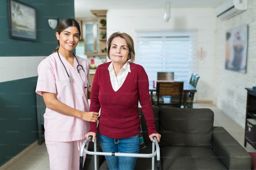 Smiling female nurse supporting senior woman standing with mobility walker at home