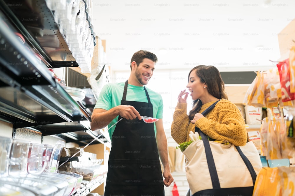 Young male worker offering food to woman for tasting in grocery store