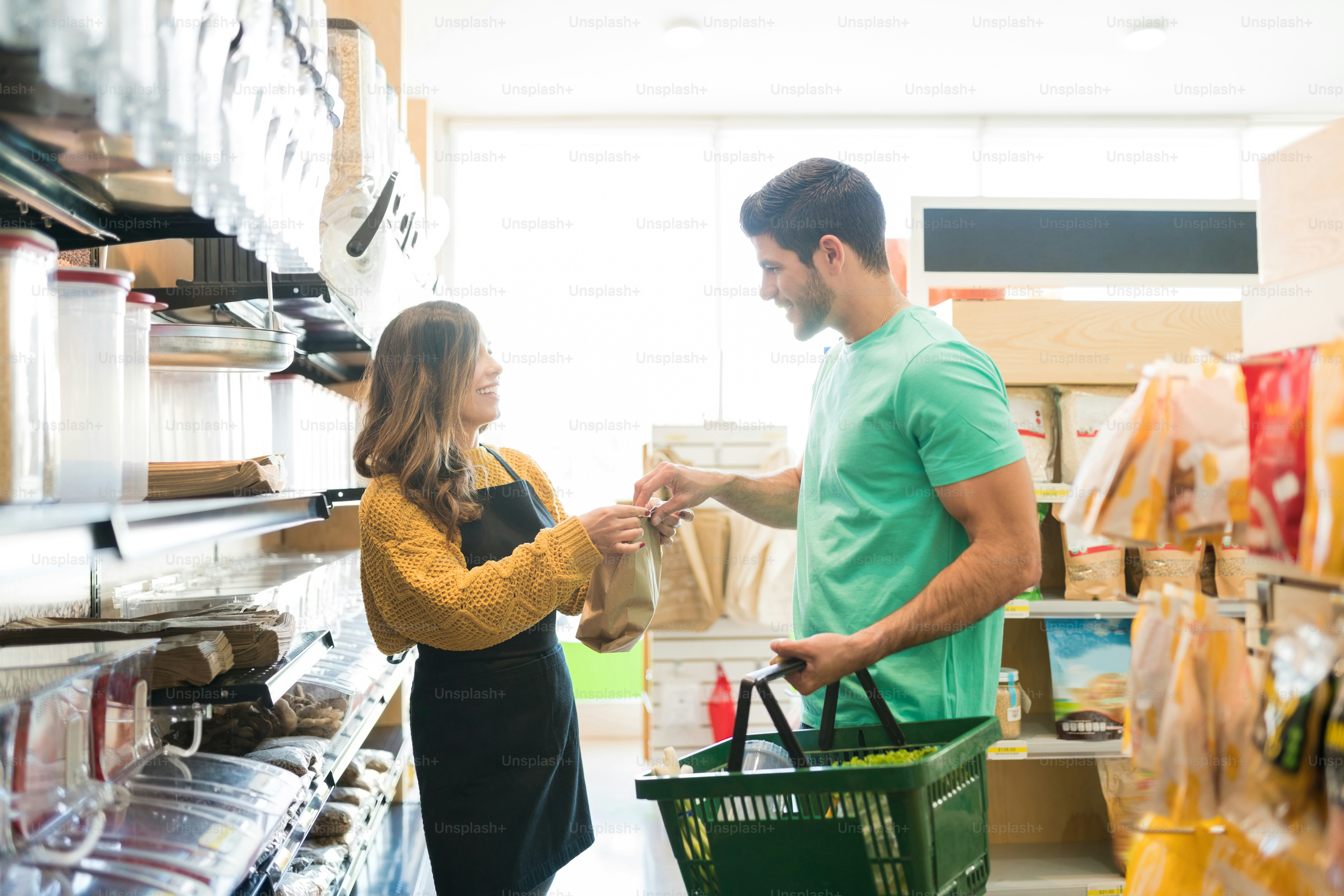 Smiling female worker giving paper bag to male customer in grocery store