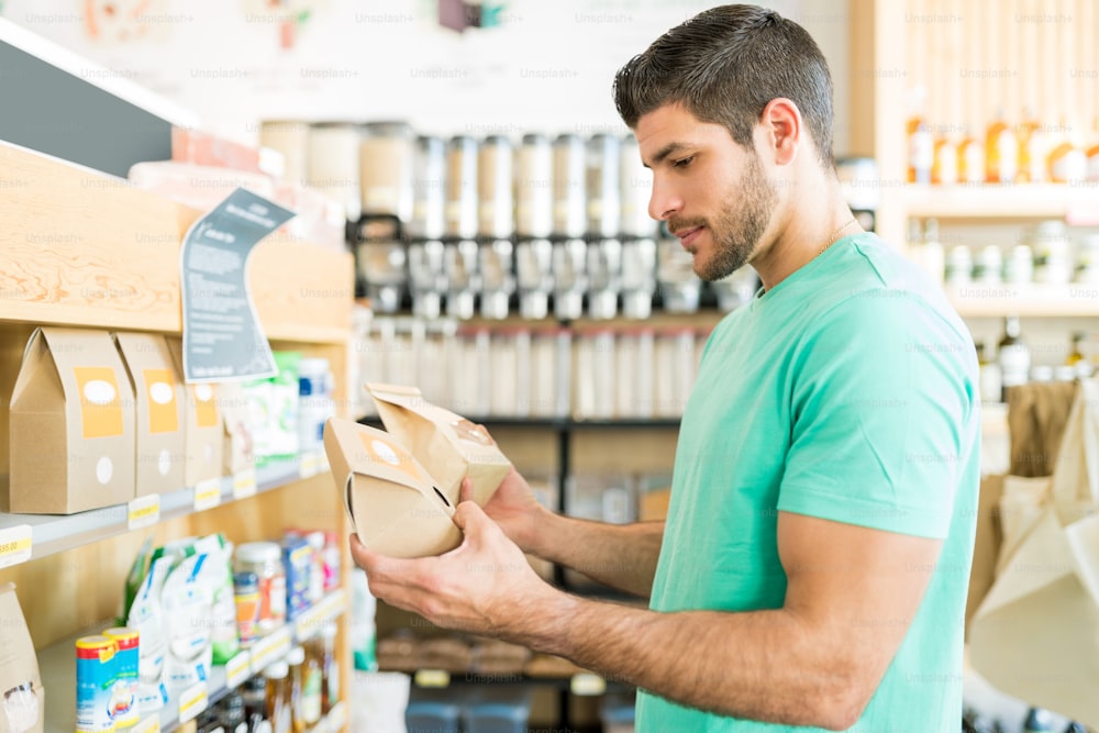 Cliente masculino guapo confundido que elige productos alimenticios en la tienda de comestibles