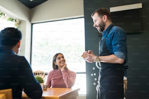 Mid adult waiter taking orders from smiling customers in restaurant