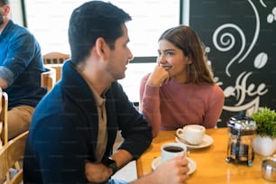 Smiling woman looking at boyfriend talking while enjoying coffee at table in restaurant