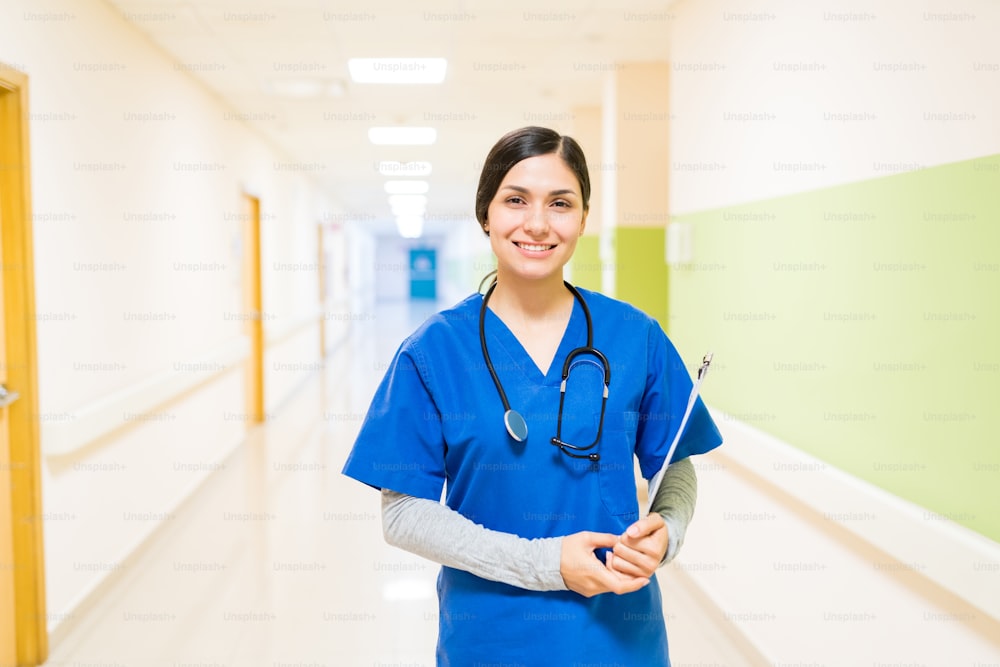 Latin young female doctor with stethoscope and clipboard wearing shrubs standing in corridor at hospital
