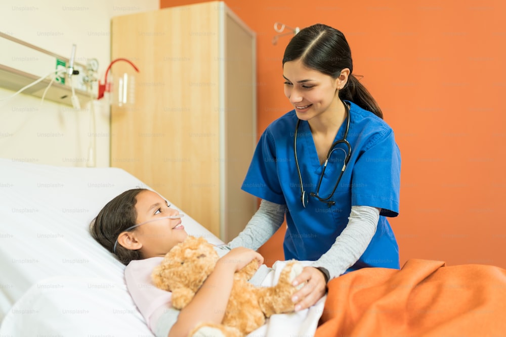Female nurse talking to little patient at hospital bed during treatment