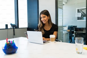 Retrato de una hermosa joven empresaria sentada con una computadora portátil en el escritorio en una oficina creativa